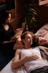 Three people relax together in a cozy bedroom setting, enjoying leisure time indoors.