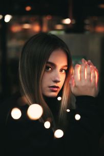 Moody portrait of a young woman holding light orbs with a dramatic and dreamy ambiance.